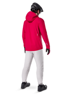 Alpinestars A-Dura Waterproof Pants in Titanium, rear view of a rider wearing the light gray technical mountain bike pants with a bright red hooded jacket and black helmet, durable waterproof gear for cycling in wet conditions