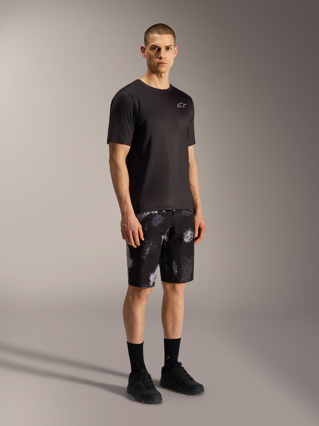 A-Dura Ride MTB-shorts in Black Camo met grijs camouflagepatroon, gecombineerd met een zwart shirt en schoenen.