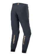 Alpinestars A-Aria Elite Broek, mountainbikebroek, zwart, achteraanzicht met gouden verticale logo's op de onderbenen, prestatiegerichte pasvorm met vochtafvoerende tailleband en zakken met rits, ontworpen voor off-road fietsen.