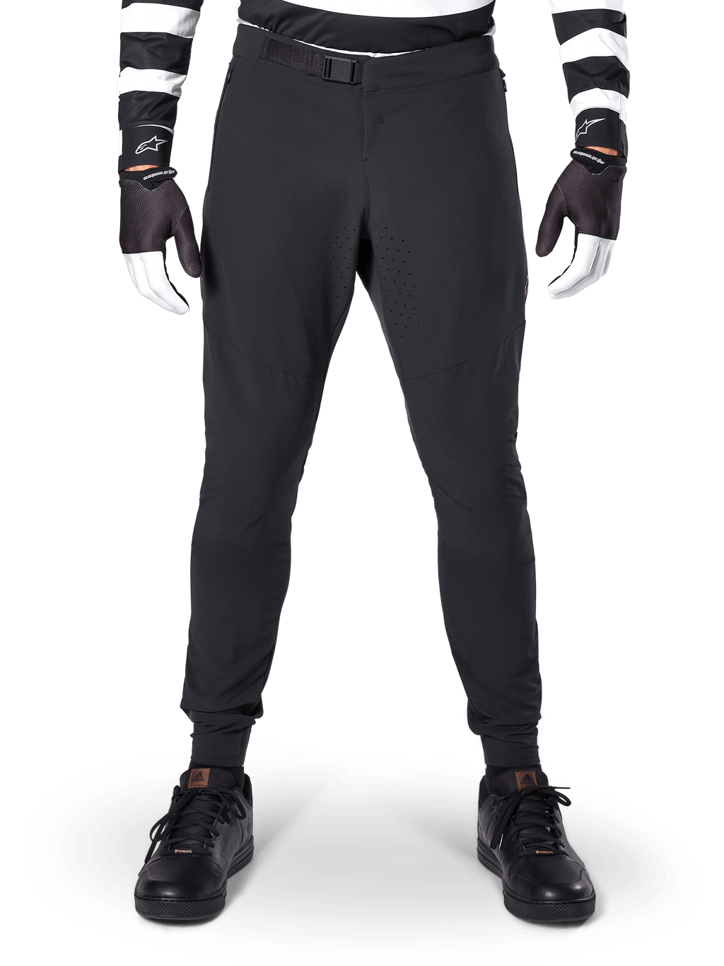 Alpinestars A-Aria Elite broek, mountainbikebroek, zwart, vooraanzicht met laserperforaties en magnetische gespsluiting, gedragen met een zwart-wit gestreepte jersey en zwarte handschoenen, hoogwaardige fietskleding voor trailrijden