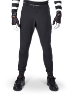 Alpinestars A-Aria Elite broek, mountainbikebroek, zwart, vooraanzicht met laserperforaties en magnetische gespsluiting, gedragen met een zwart-wit gestreepte jersey en zwarte handschoenen, hoogwaardige fietskleding voor trailrijden