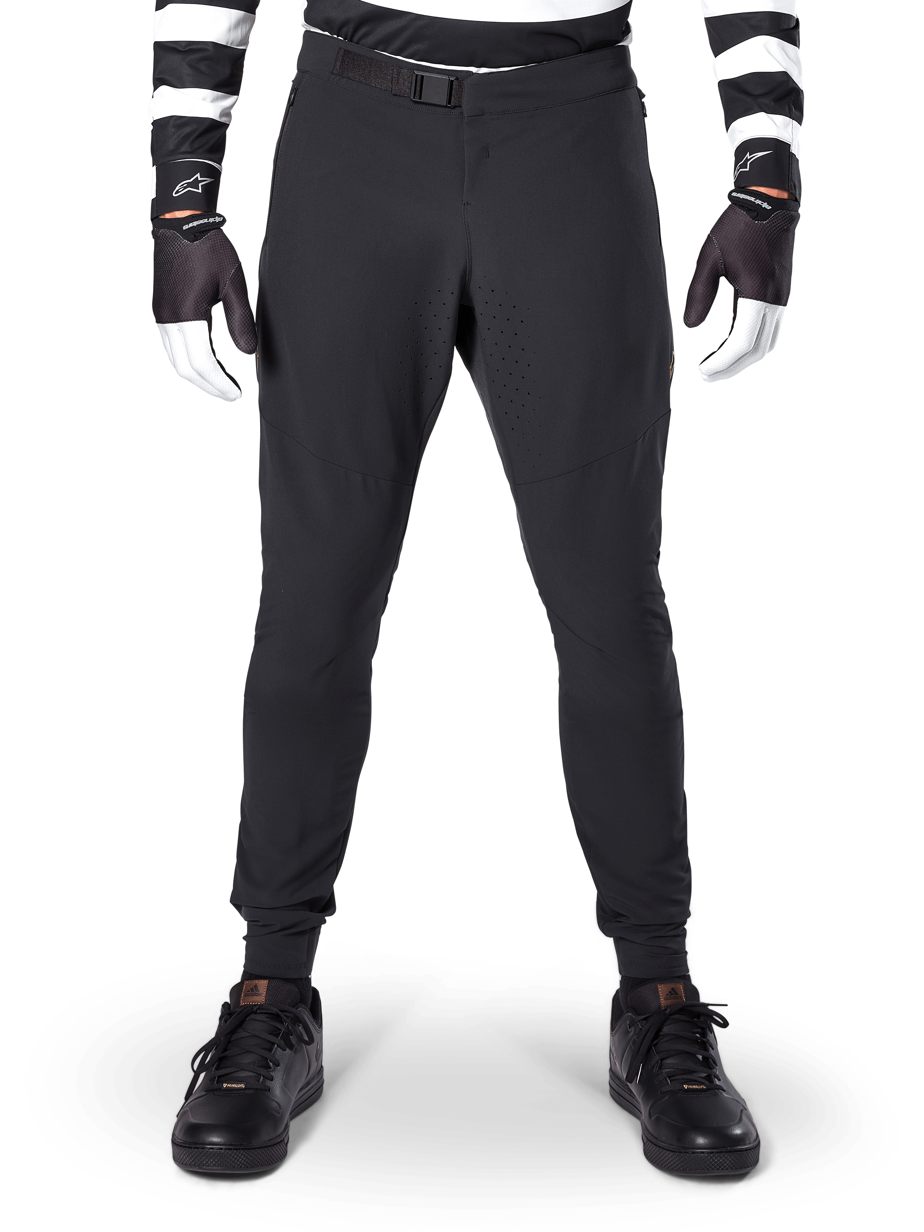 Alpinestars A-Aria Elite broek, mountainbikebroek, zwart, vooraanzicht met laserperforaties en magnetische gespsluiting, gedragen met een zwart-wit gestreepte jersey en zwarte handschoenen, hoogwaardige fietskleding voor trailrijden