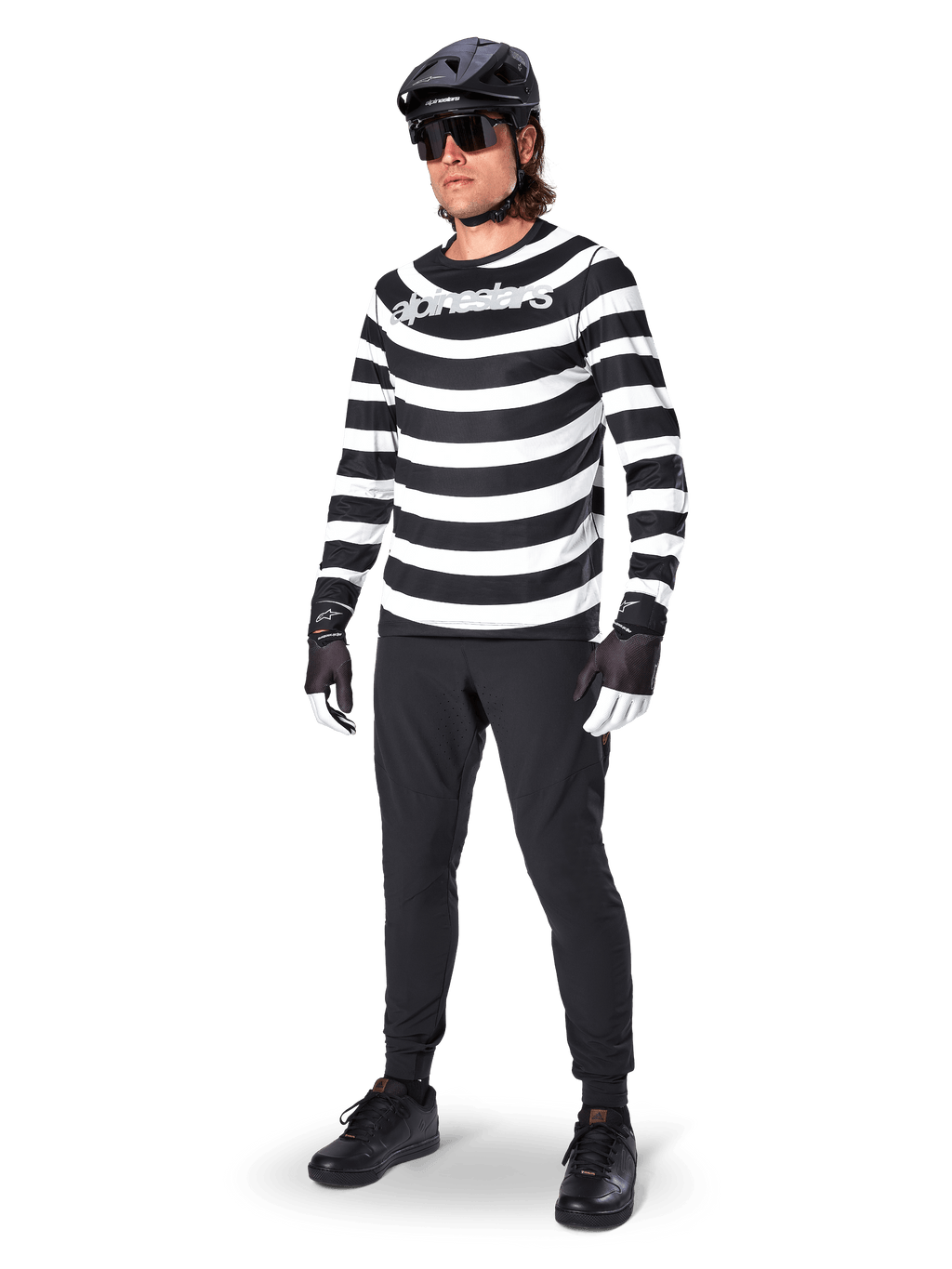 Alpinestars A-Aria Elite broek, zwarte MTB-broek, gedragen door een rijder met een zwart-wit gestreept shirt met lange mouwen, zwarte helm, zonnebril en zwart-witte handschoenen, performancekleding voor off-road fietsen