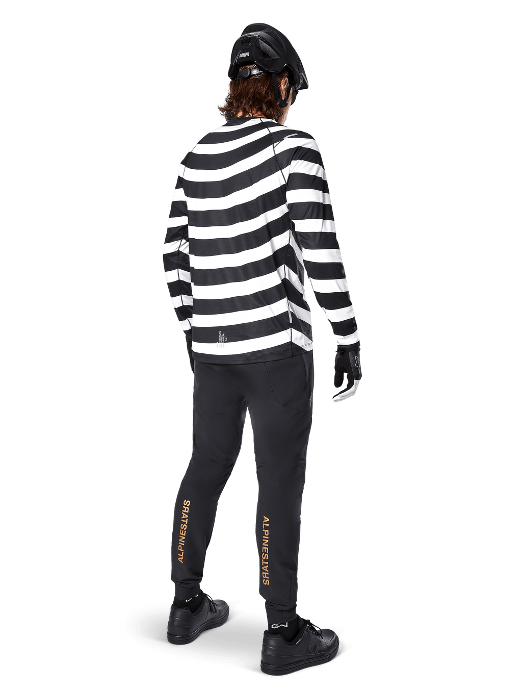Alpinestars A-Aria Elite Pants, zwarte MTB-broek, met verticaal goudkleurig logo op de kuiten, gedragen door een rijder met een zwart-wit gestreepte jersey met lange mouwen, zwarte helm en zwarte schoenen, achteraanzicht toont de prestatiegerichte pasvorm en het trail-ready ontwerp