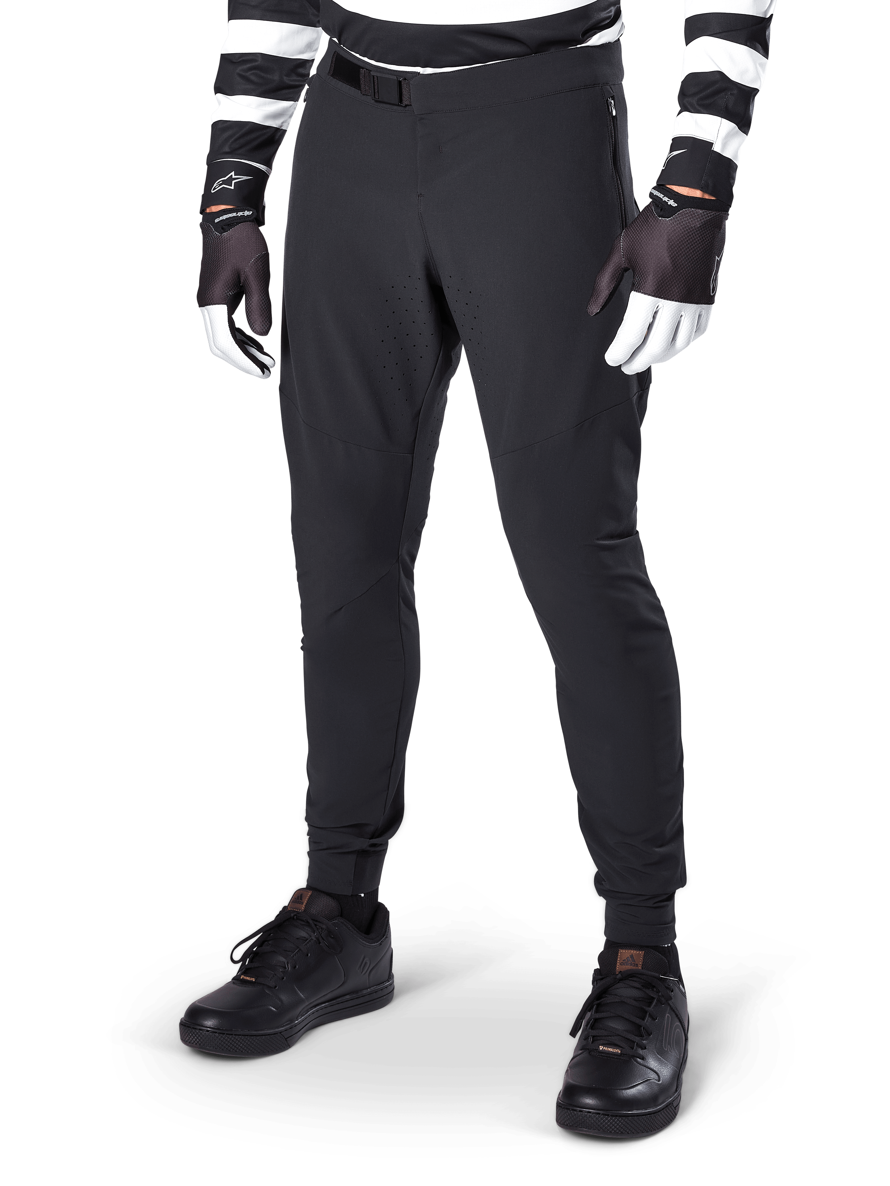 Alpinestars A-Aria Elite broek, zwarte mountainbikebroek, met lasergesneden ventilatie op de dijen en magnetische gespsluiting, gedragen met zwart-wit gestreepte jersey en handschoenen, performance MTB-kleding voor off-road fietsen