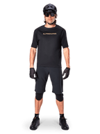 Mannelijke mountainbiker die zwarte Alpinestars A-Aria Elite Shorts draagt, gecombineerd met een bijpassend zwart Alpinestars fietsshirt met korte mouwen, zwarte helm, handschoenen en kniebeschermers, complete off-road wieleroutfit