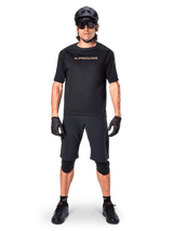Mannelijke mountainbiker die zwarte Alpinestars A-Aria Elite Shorts draagt, gecombineerd met een bijpassend zwart Alpinestars fietsshirt met korte mouwen, zwarte helm, handschoenen en kniebeschermers, complete off-road wieleroutfit