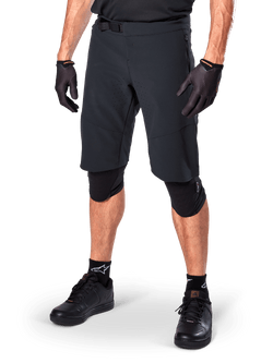 Alpinestars A-Aria Elite Shorts, Black Cycling Shorts, worn with matching black gloves and knee guards, featuring a magnetic buckle and laser-cut perforations, sleek design for off-road mountain biking
