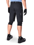 Alpinestars A-Dura Elite Shorts, zwart, achteraanzicht van een rijder in mountainbike-uitrusting inclusief zwarte kniebeschermers, handschoenen en sokken met witte logo's, voorzien van zijzakken met ritssluiting en reflecterende accenten op duurzame Cordura-stof.