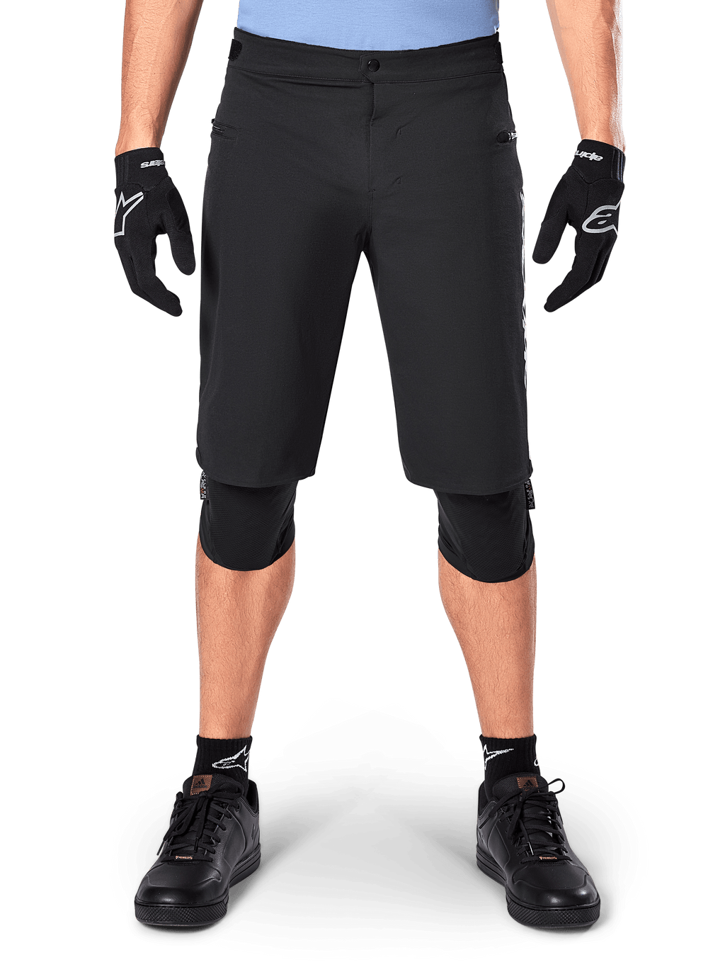 Alpinestars A-Dura Elite Shorts, zwarte mountainbike short, gedragen door een rijder met zwarte handschoenen en kniebeschermers, met drukknoopsluiting aan de voorzijde en ritszakken, duurzaam Cordura-materiaal voor off-road fietsen