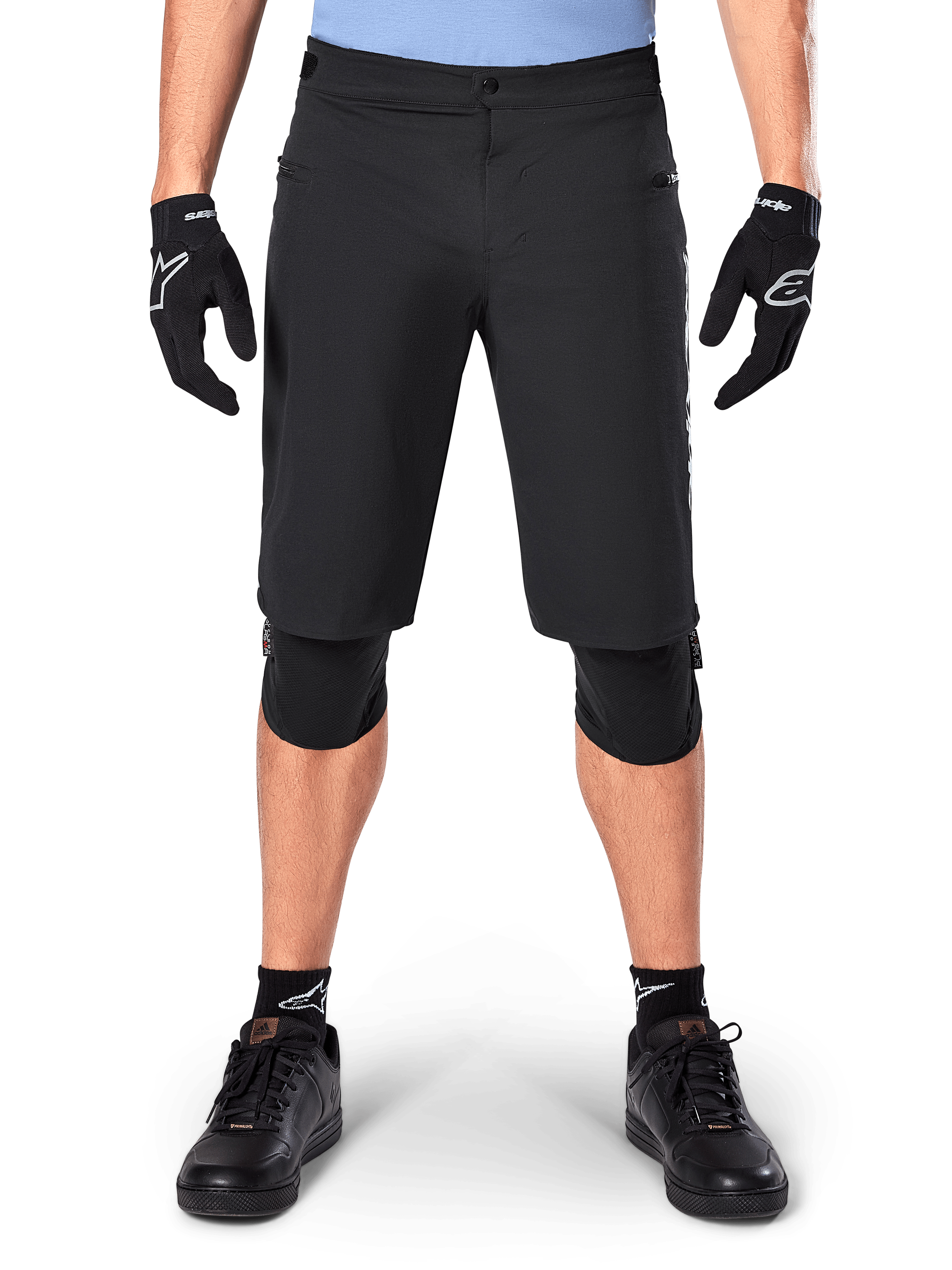Alpinestars A-Dura Elite Shorts, zwarte mountainbike short, gedragen door een rijder met zwarte handschoenen en kniebeschermers, met drukknoopsluiting aan de voorzijde en ritszakken, duurzaam Cordura-materiaal voor off-road fietsen