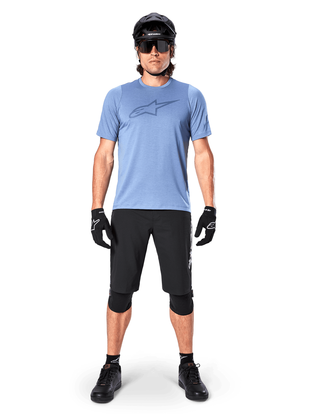 Alpinestars A-Dura Elite Shorts, zwarte mountainbike shorts, gedragen met een lichtblauw t-shirt, zwarte helm, zonnebril en kniebeschermers, professionele off-road fietskleding
