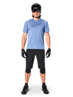 Alpinestars A-Dura Elite Shorts, zwarte mountainbike shorts, gedragen met een lichtblauw t-shirt, zwarte helm, zonnebril en kniebeschermers, professionele off-road fietskleding