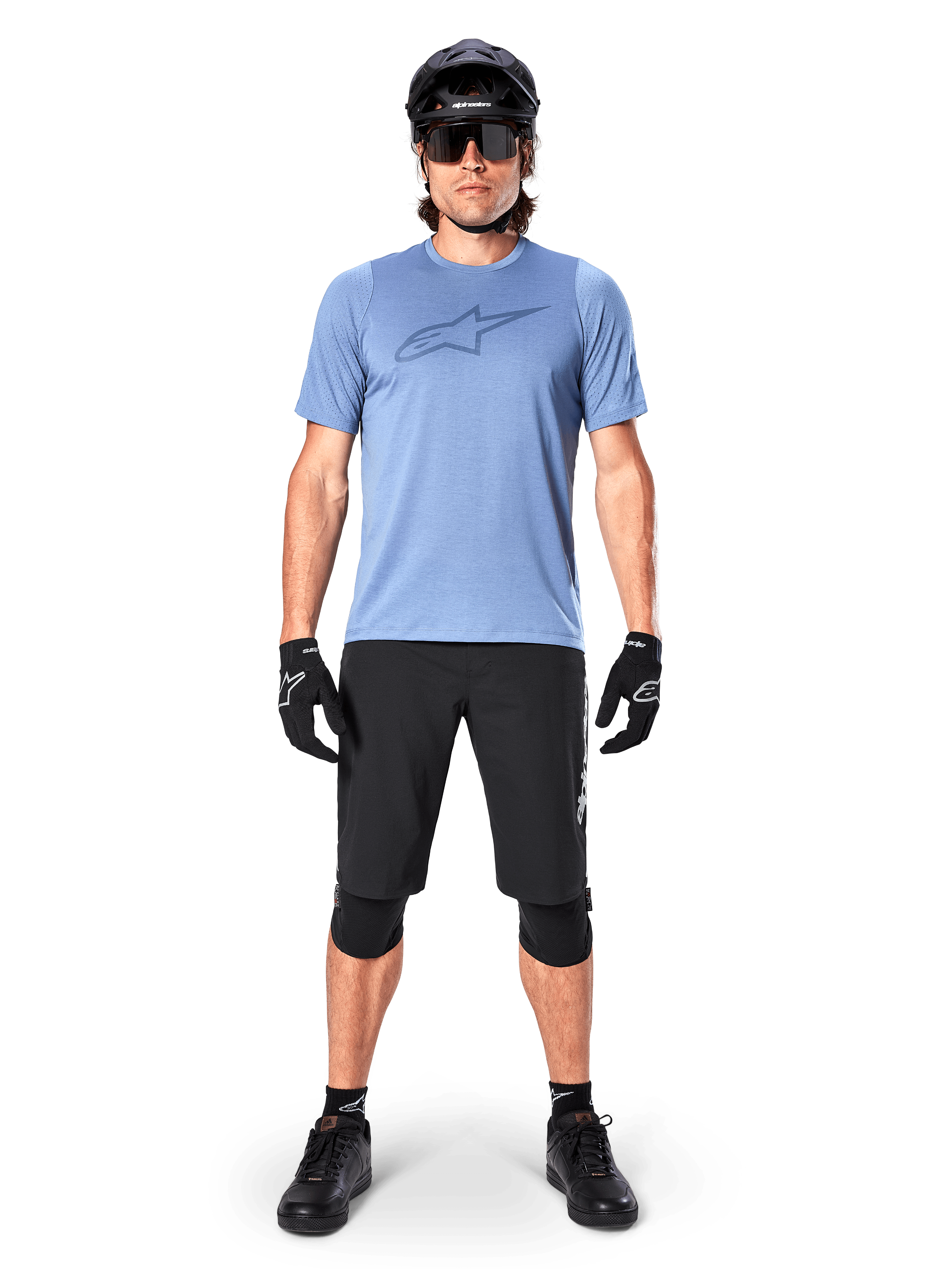 Alpinestars A-Dura Elite Shorts, zwarte mountainbike shorts, gedragen met een lichtblauw t-shirt, zwarte helm, zonnebril en kniebeschermers, professionele off-road fietskleding