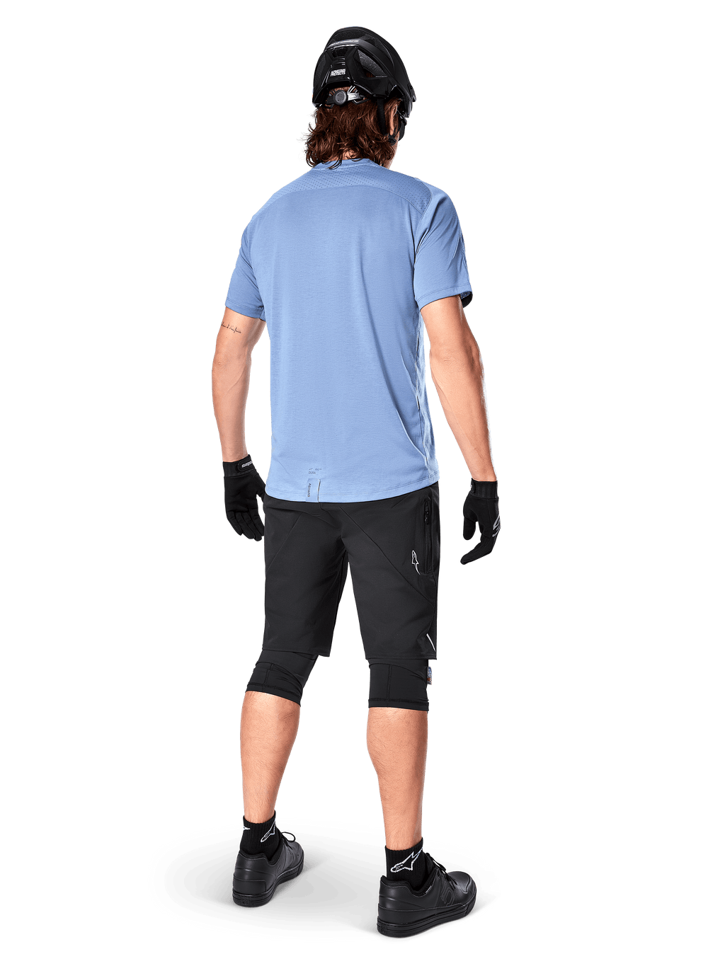 Alpinestars A-Dura Elite Shorts, mountainbikebroek, zwart, achteraanzicht op model, gedragen met lichtblauw shirt met korte mouwen en zwarte beschermende uitrusting, technisch ontwerp met ritszakken en reflecterende details voor off-road fietsen
