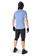 Alpinestars A-Dura Elite Shorts, mountainbikebroek, zwart, achteraanzicht op model, gedragen met lichtblauw shirt met korte mouwen en zwarte beschermende uitrusting, technisch ontwerp met ritszakken en reflecterende details voor off-road fietsen