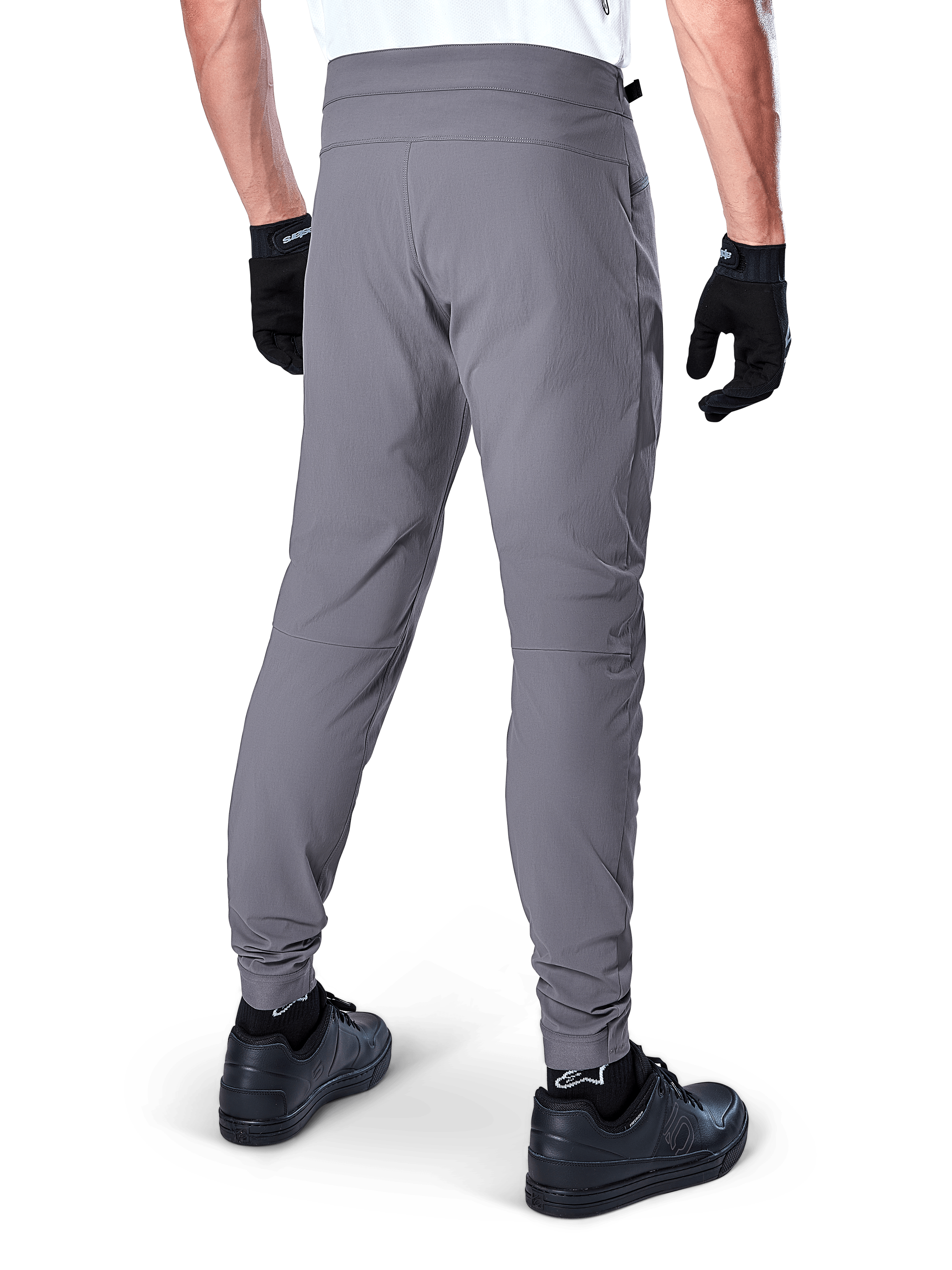Alpinestars A-Dura Pants, mountainbikebroek, donkergrijs, achteraanzicht van model die de kleding draagt, voorzien van een duurzame 2-way stretchstof en elastische boorden, gecombineerd met zwarte handschoenen en sneakers voor een complete fietslook