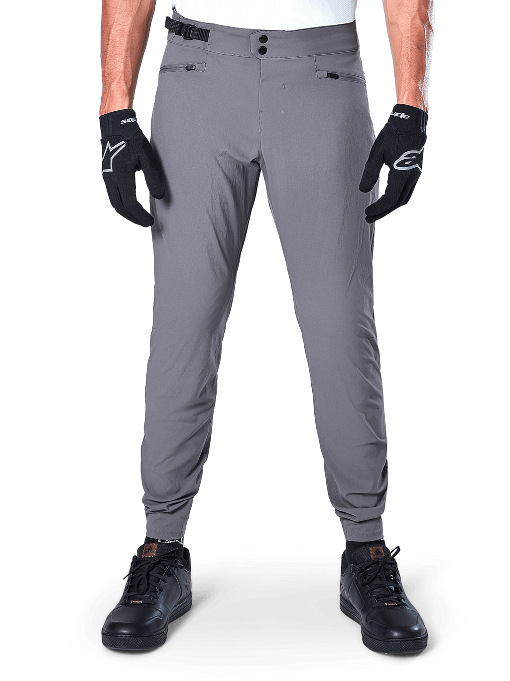 Alpinestars A-Dura Pants, donkergrijze mountainbikebroek, vooraanzicht gedragen met zwarte handschoenen en zwarte sneakers, met dubbele drukknoopsluiting bij de taille, handzakken met rits en elastische manchetten, duurzame fietskleding voor trailrijden