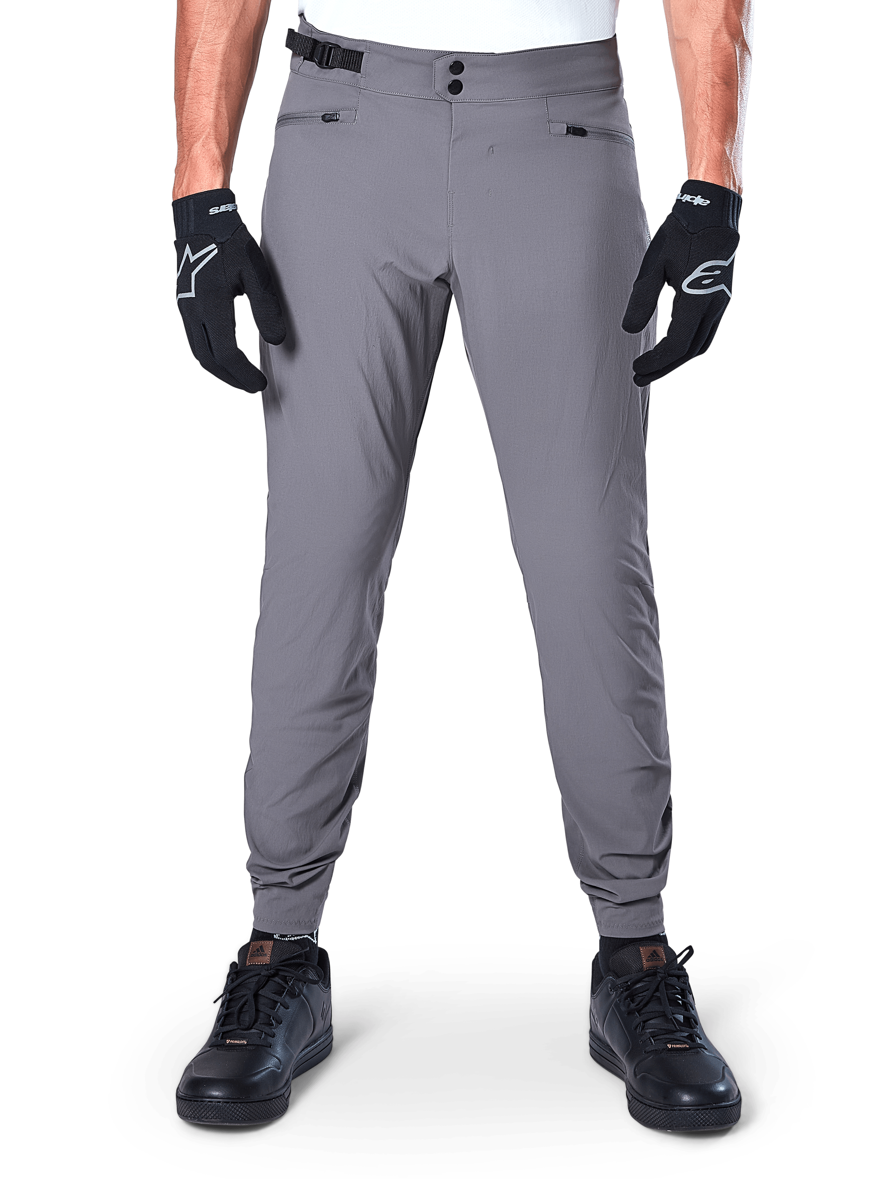 Alpinestars A-Dura Pants, donkergrijze mountainbikebroek, vooraanzicht gedragen met zwarte handschoenen en zwarte sneakers, met dubbele drukknoopsluiting bij de taille, handzakken met rits en elastische manchetten, duurzame fietskleding voor trailrijden