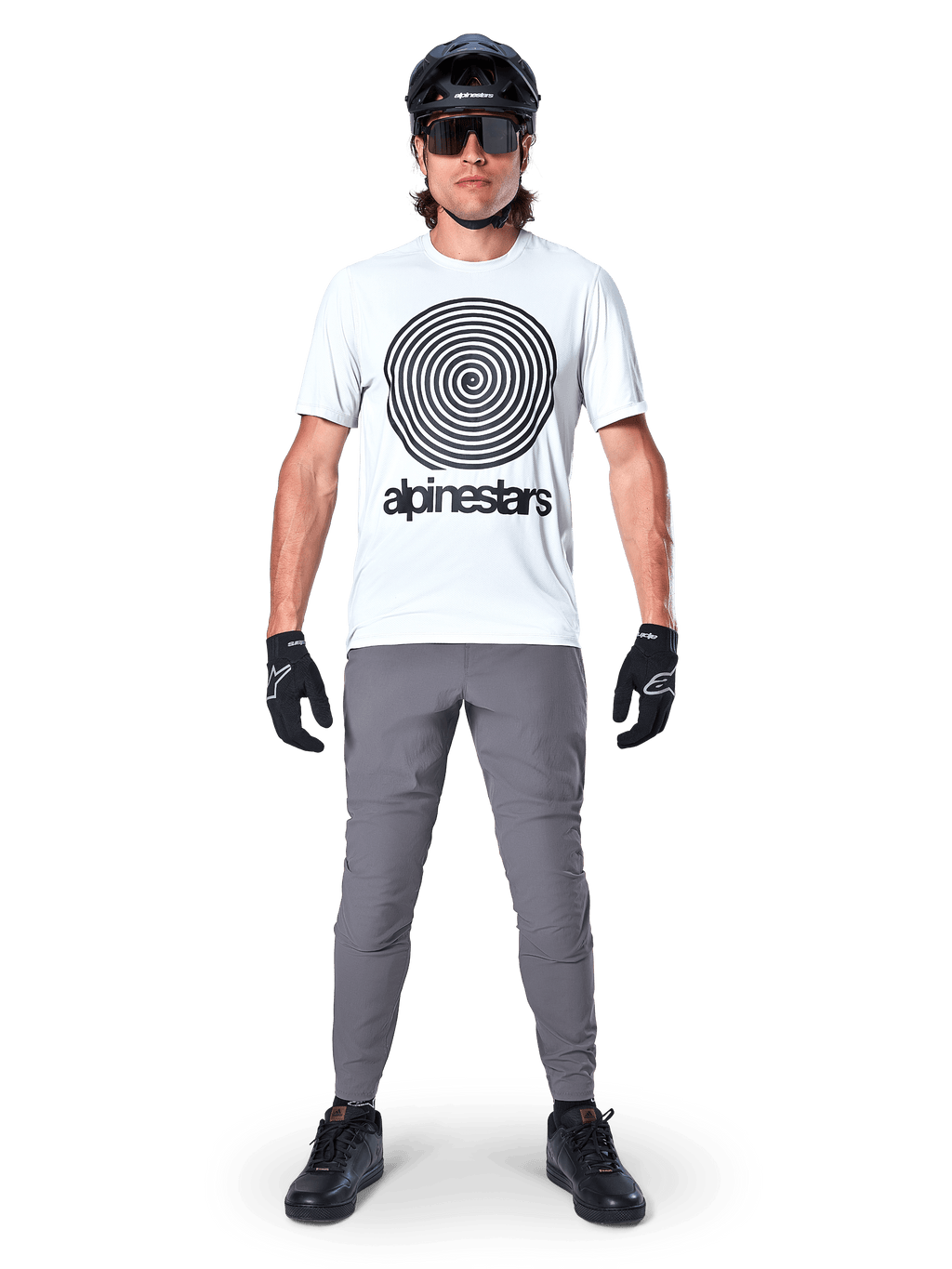Alpinestars A-Dura Pants, MTB-fietsbroek, donkergrijs, gedragen met een wit grafisch t-shirt, zwarte helm en handschoenen, met een duurzaam 2-way stretch-ontwerp en regular fit voor mountainbiken