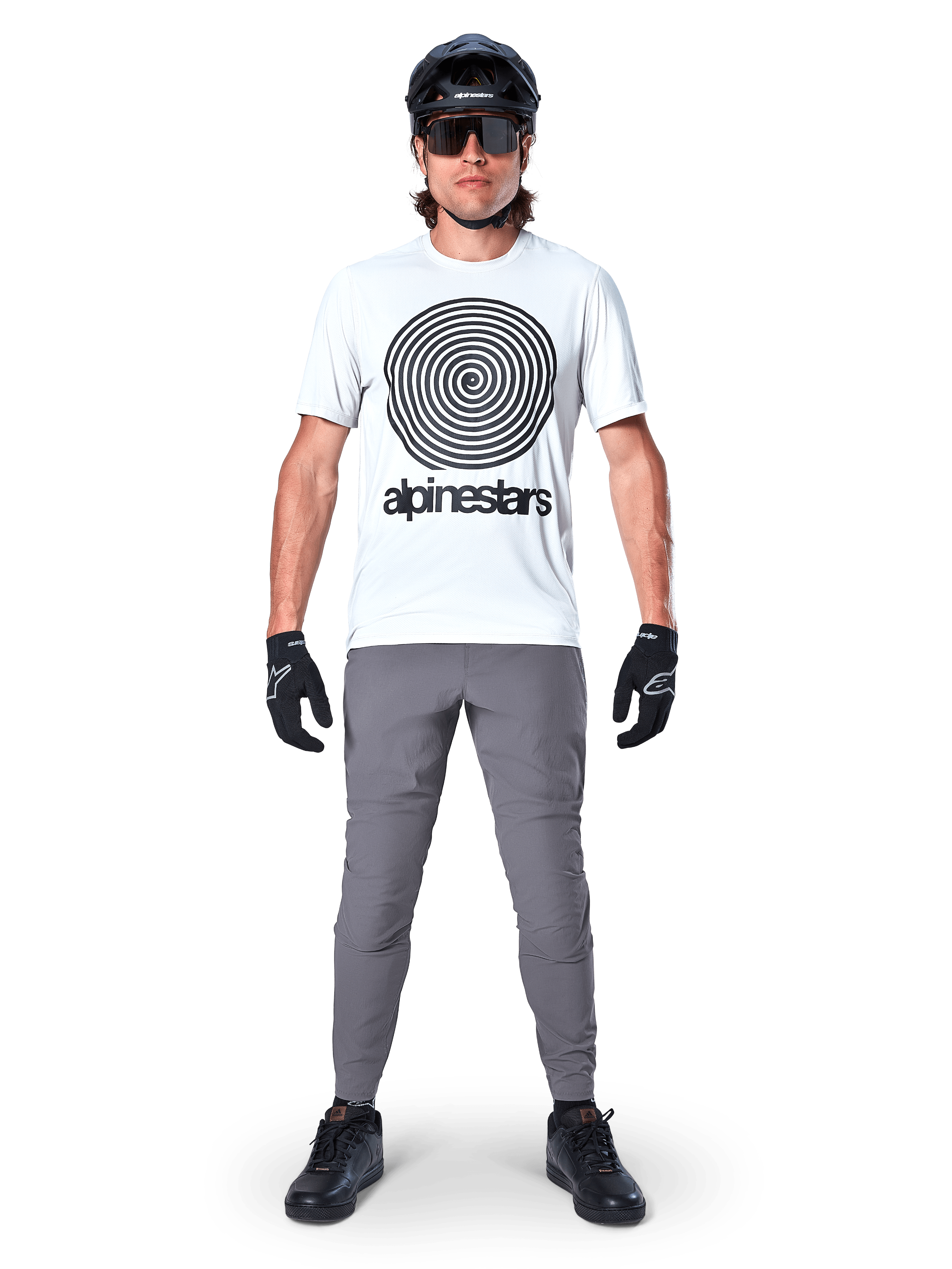 Alpinestars A-Dura Pants, MTB-fietsbroek, donkergrijs, gedragen met een wit grafisch t-shirt, zwarte helm en handschoenen, met een duurzaam 2-way stretch-ontwerp en regular fit voor mountainbiken