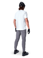 Alpinestars A-Dura broek, donkergrijze mountainbikebroek van achteren gezien, gedragen met een wit T-shirt met korte mouwen, zwarte MTB-helm, zwarte handschoenen en schoenen, regular fit ontwerp met elastische manchetten, duurzame off-road fietskleding