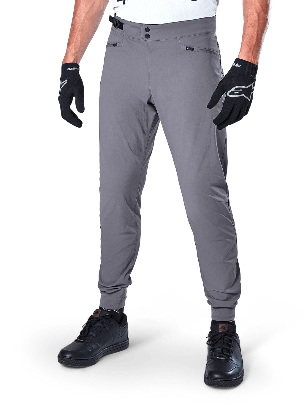 Alpinestars A-Dura broek, donkergrijze MTB-broek, voorzien van een dubbele drukknoopsluiting en zakken met ritssluiting, elastische manchetten, gedragen met zwarte fietshandschoenen en zwarte sneakers