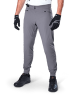Alpinestars A-Dura broek, donkergrijze MTB-broek, voorzien van een dubbele drukknoopsluiting en zakken met ritssluiting, elastische manchetten, gedragen met zwarte fietshandschoenen en zwarte sneakers