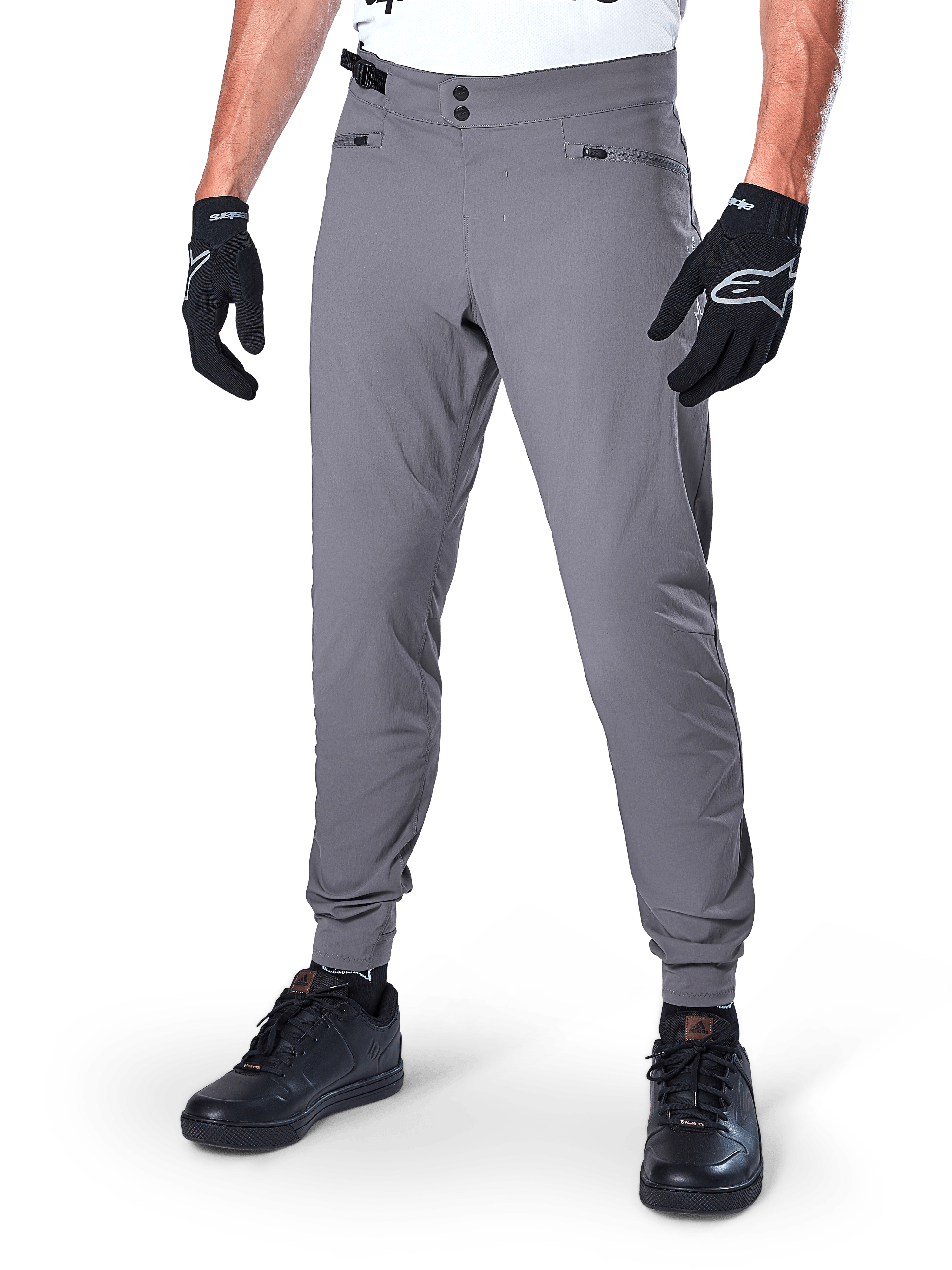 Alpinestars A-Dura broek, donkergrijze MTB-broek, voorzien van een dubbele drukknoopsluiting en zakken met ritssluiting, elastische manchetten, gedragen met zwarte fietshandschoenen en zwarte sneakers