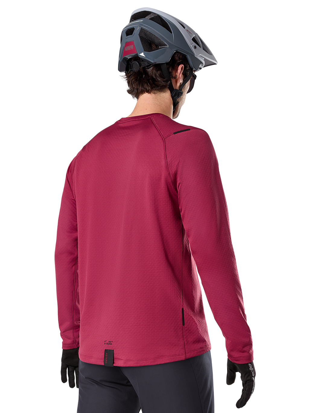 Alpinestars A-Dura Thermal Jersey, MTB-shirt met lange mouwen, bordeauxrood, achteraanzicht op model met een grijze MTB-helm en zwarte handschoenen, voorzien van een verlengde achterkant en kleine logo-details, ontworpen voor trailrijden in koud weer.