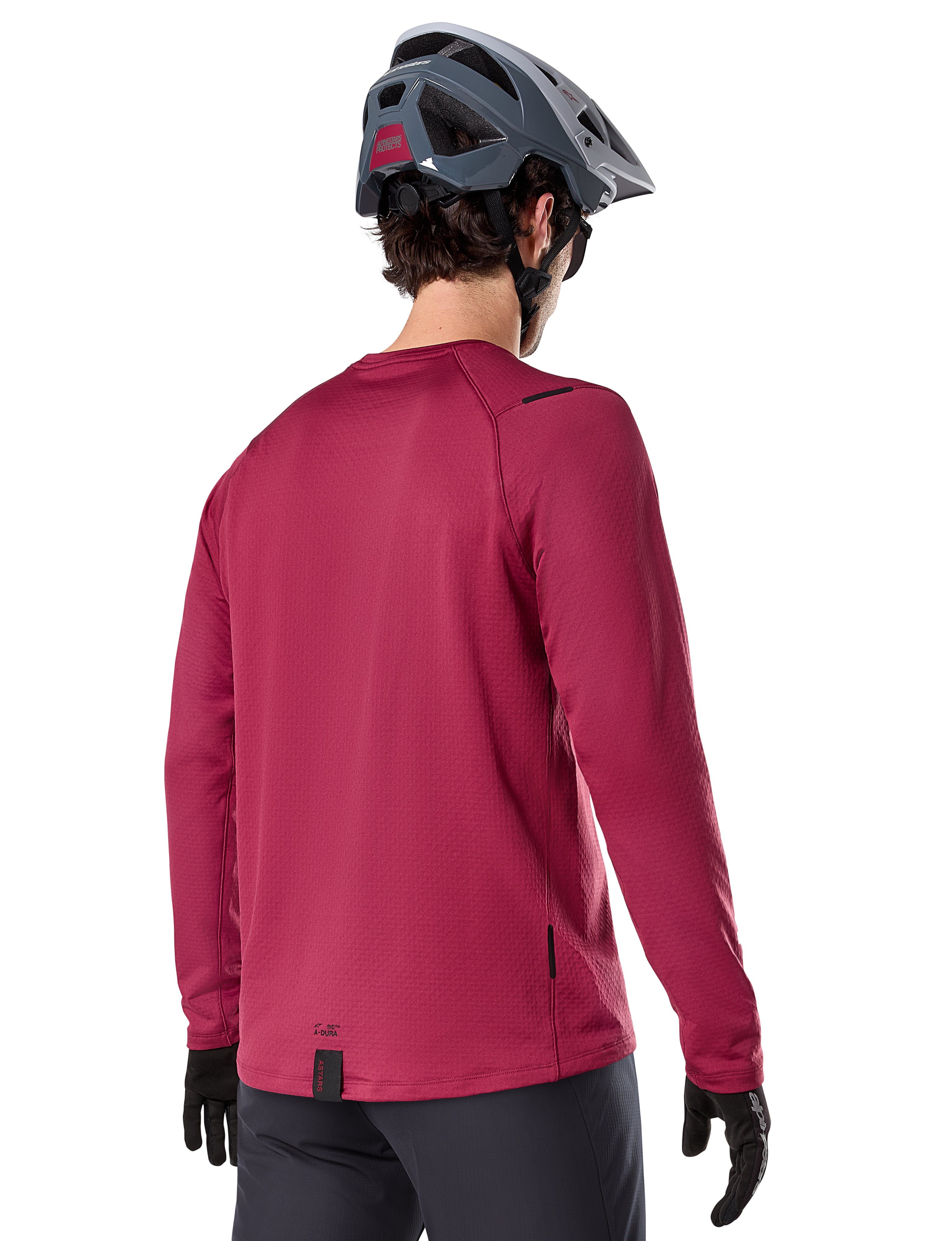 Alpinestars A-Dura Thermal Jersey, MTB-shirt met lange mouwen, bordeauxrood, achteraanzicht op model met een grijze MTB-helm en zwarte handschoenen, voorzien van een verlengde achterkant en kleine logo-details, ontworpen voor trailrijden in koud weer.