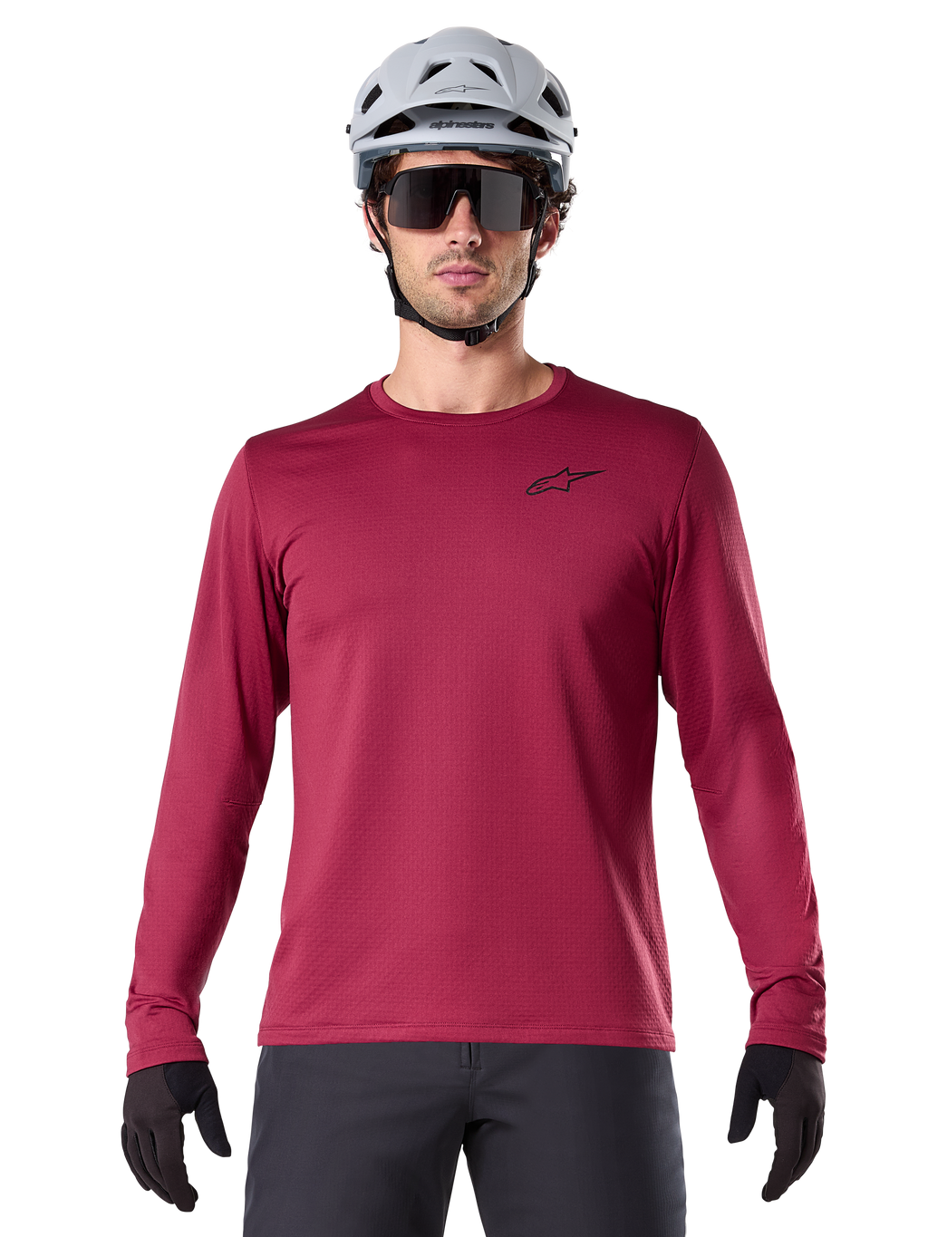 Mannelijke fietser in Alpinestars A-Dura Thermal Jersey, MTB-shirt met lange mouwen, bordeauxrood, gecombineerd met een grijze helm en zwarte zonnebril, voorzien van een klein zwart sterlogo op de borst, geïsoleerde fleece-stof voor mountainbiken in koud weer
