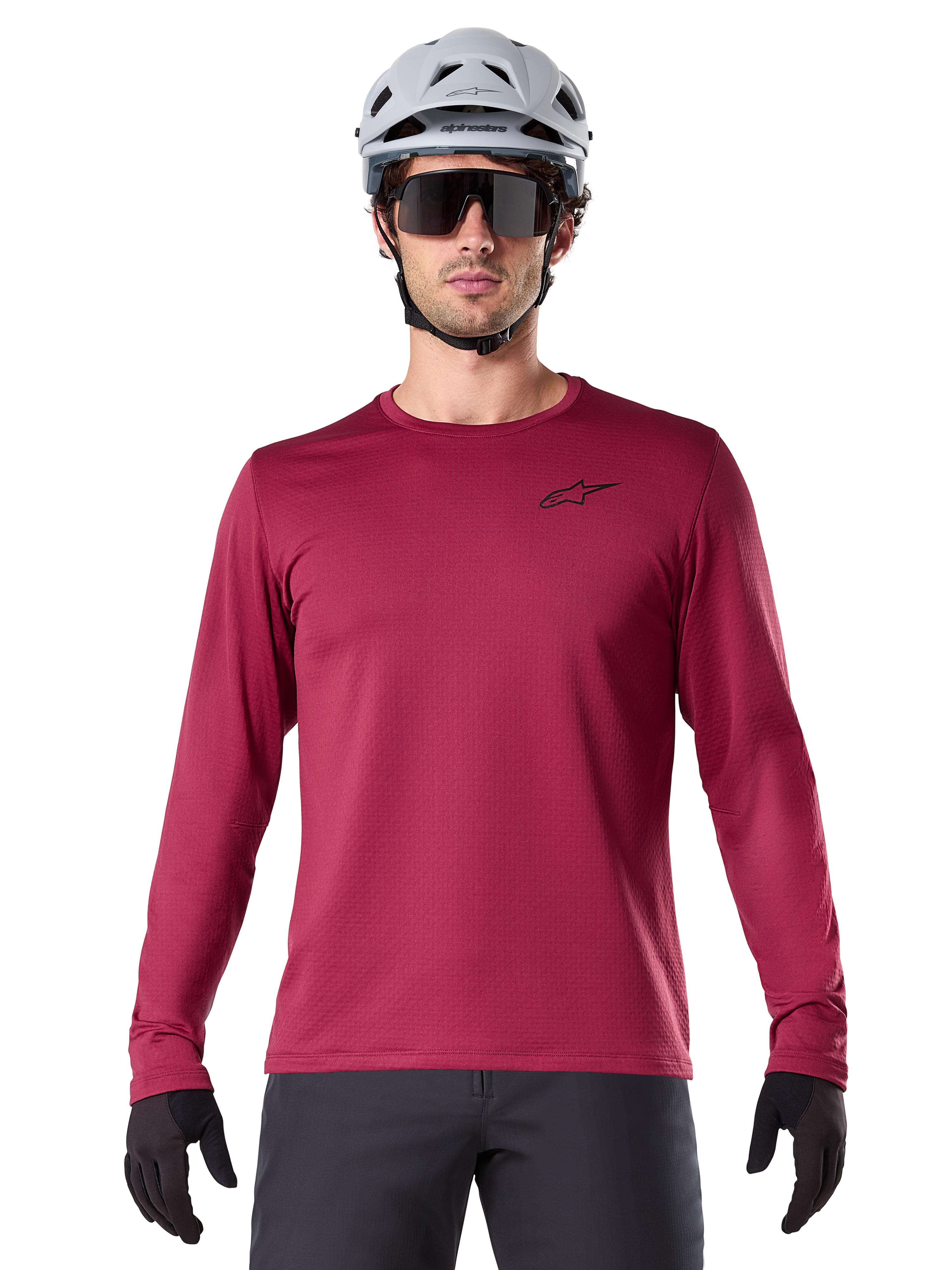 Mannelijke fietser in Alpinestars A-Dura Thermal Jersey, MTB-shirt met lange mouwen, bordeauxrood, gecombineerd met een grijze helm en zwarte zonnebril, voorzien van een klein zwart sterlogo op de borst, geïsoleerde fleece-stof voor mountainbiken in koud weer
