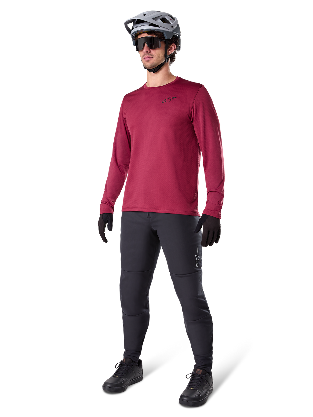 Alpinestars A-Dura Thermal Jersey in burgundy, geïsoleerd mountainbikeshirt met lange mouwen, gedragen met een donkergrijze mountainbikebroek, zwarte handschoenen en een grijze helm, studio-opname van volledige MTB-uitrusting voor koud weer.