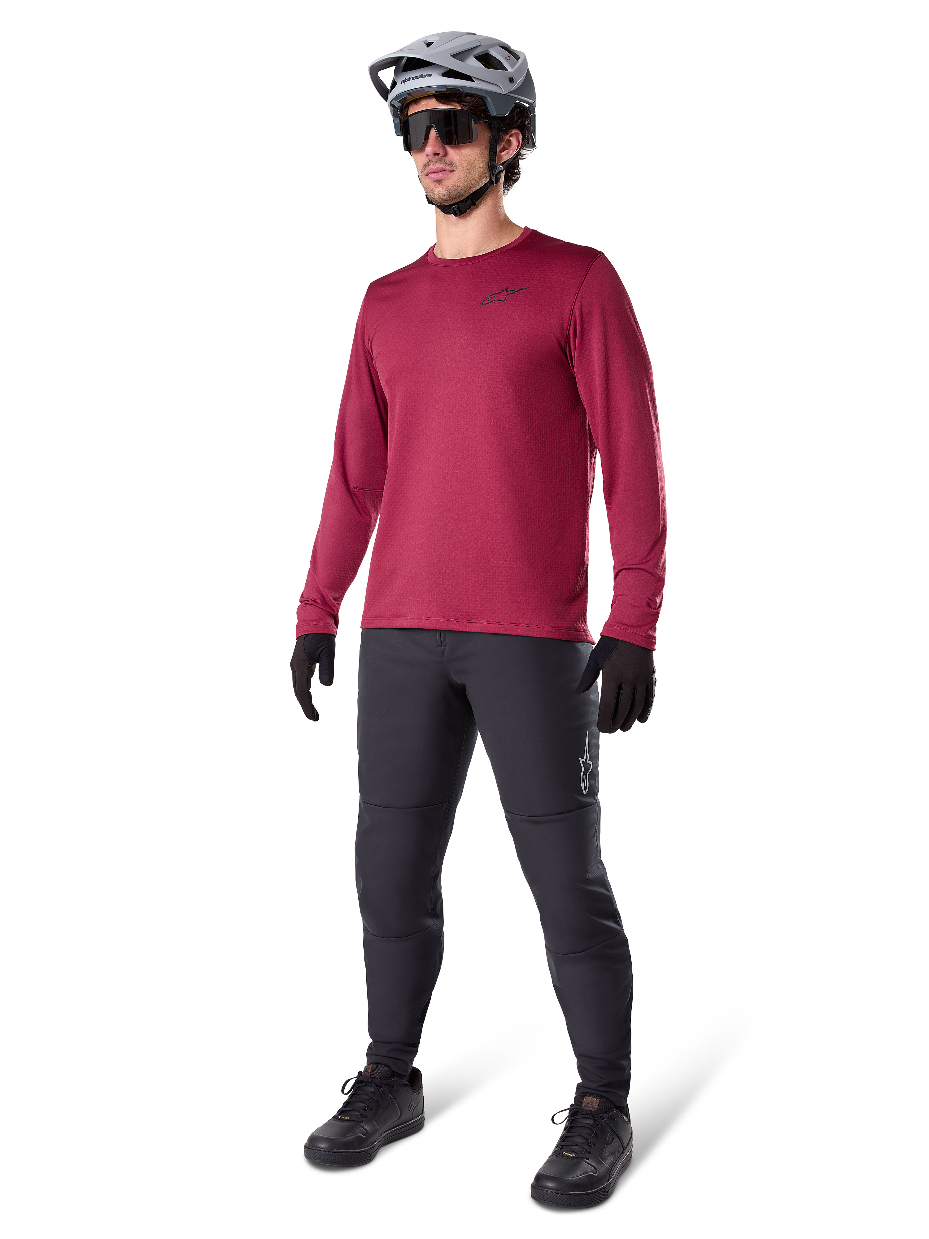Alpinestars A-Dura Thermal Jersey in burgundy, geïsoleerd mountainbikeshirt met lange mouwen, gedragen met een donkergrijze mountainbikebroek, zwarte handschoenen en een grijze helm, studio-opname van volledige MTB-uitrusting voor koud weer.