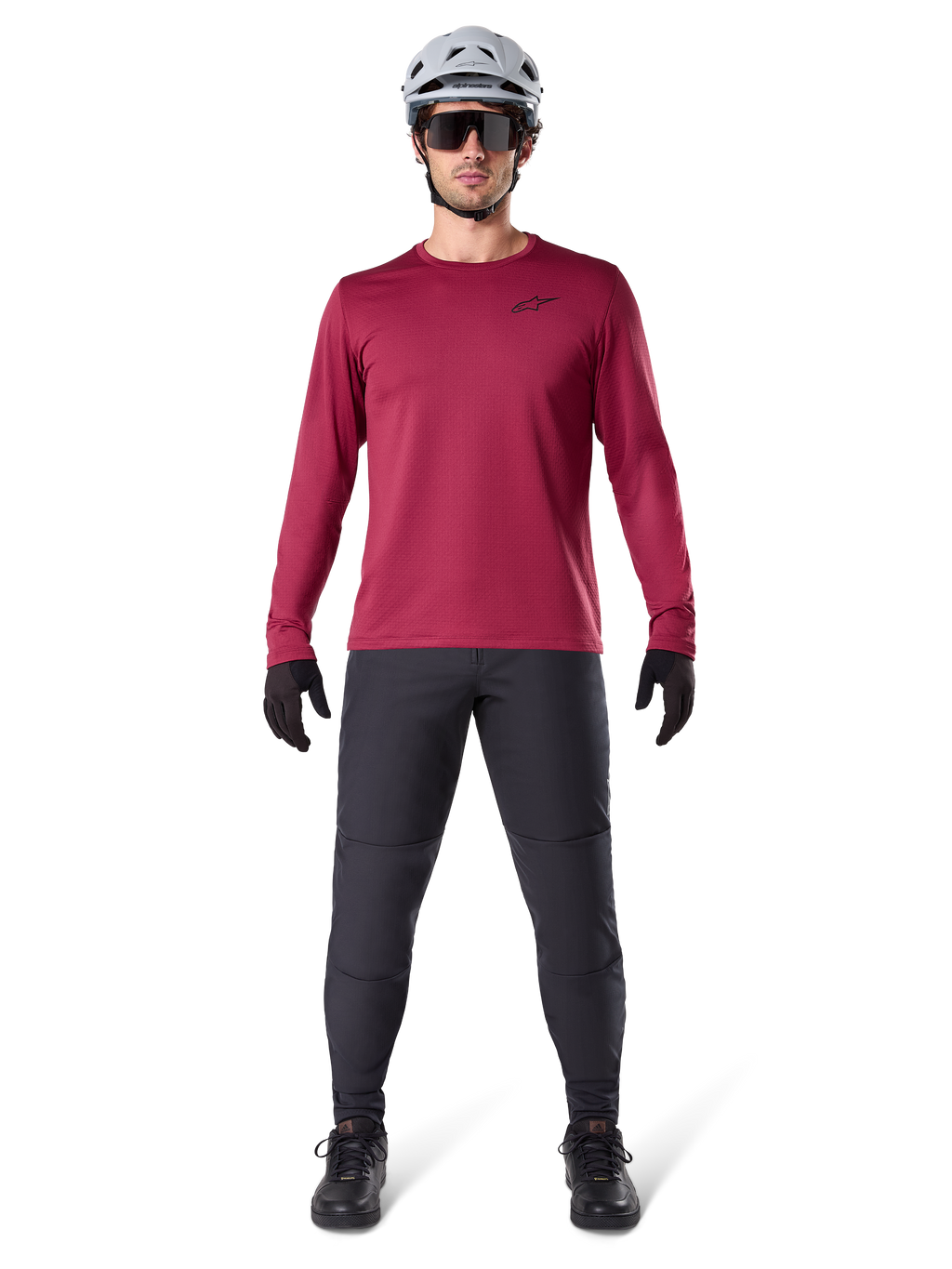 Alpinestars A-Dura Thermal Jersey in Burgundy, geïsoleerd fietsshirt met lange mouwen, mannelijk model met donkergrijze mountainbikebroek, witte helm, zwarte zonnebril en zwarte handschoenen, professionele MTB-uitrusting voor koud weer