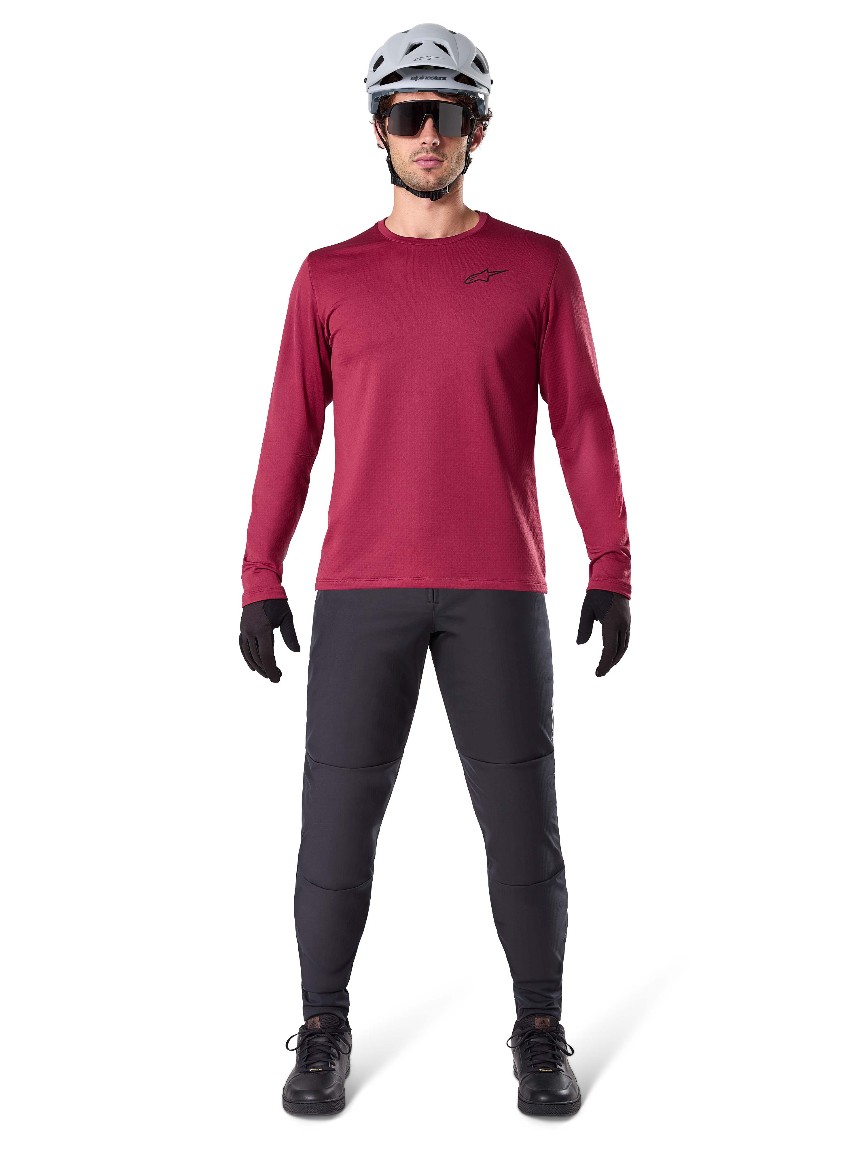 Alpinestars A-Dura Thermal Jersey in Burgundy, geïsoleerd fietsshirt met lange mouwen, mannelijk model met donkergrijze mountainbikebroek, witte helm, zwarte zonnebril en zwarte handschoenen, professionele MTB-uitrusting voor koud weer