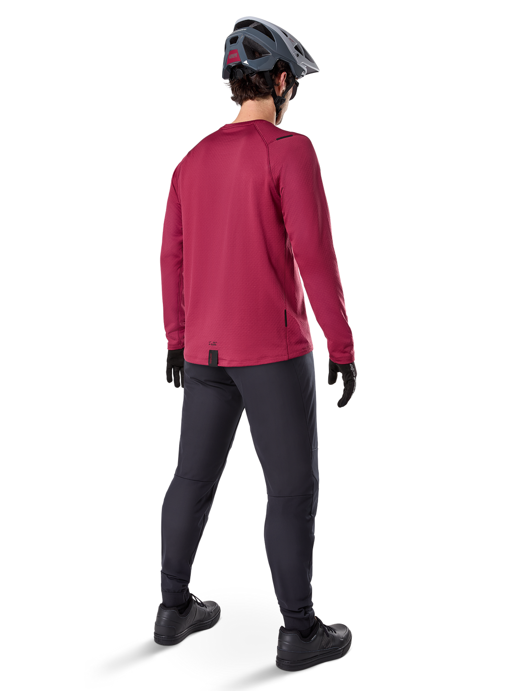 Alpinestars A-Dura Thermal Jersey, bordeauxrood wielershirt met lange mouwen, achteraanzicht, gedragen met een zwarte mountainbikebroek en een grijze helm, voorzien van een verlengde achterzoom voor extra dekking aan de achterkant, mountainbike-uitrusting voor koud weer