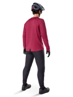 Alpinestars A-Dura Thermal Jersey, bordeauxrood wielershirt met lange mouwen, achteraanzicht, gedragen met een zwarte mountainbikebroek en een grijze helm, voorzien van een verlengde achterzoom voor extra dekking aan de achterkant, mountainbike-uitrusting voor koud weer