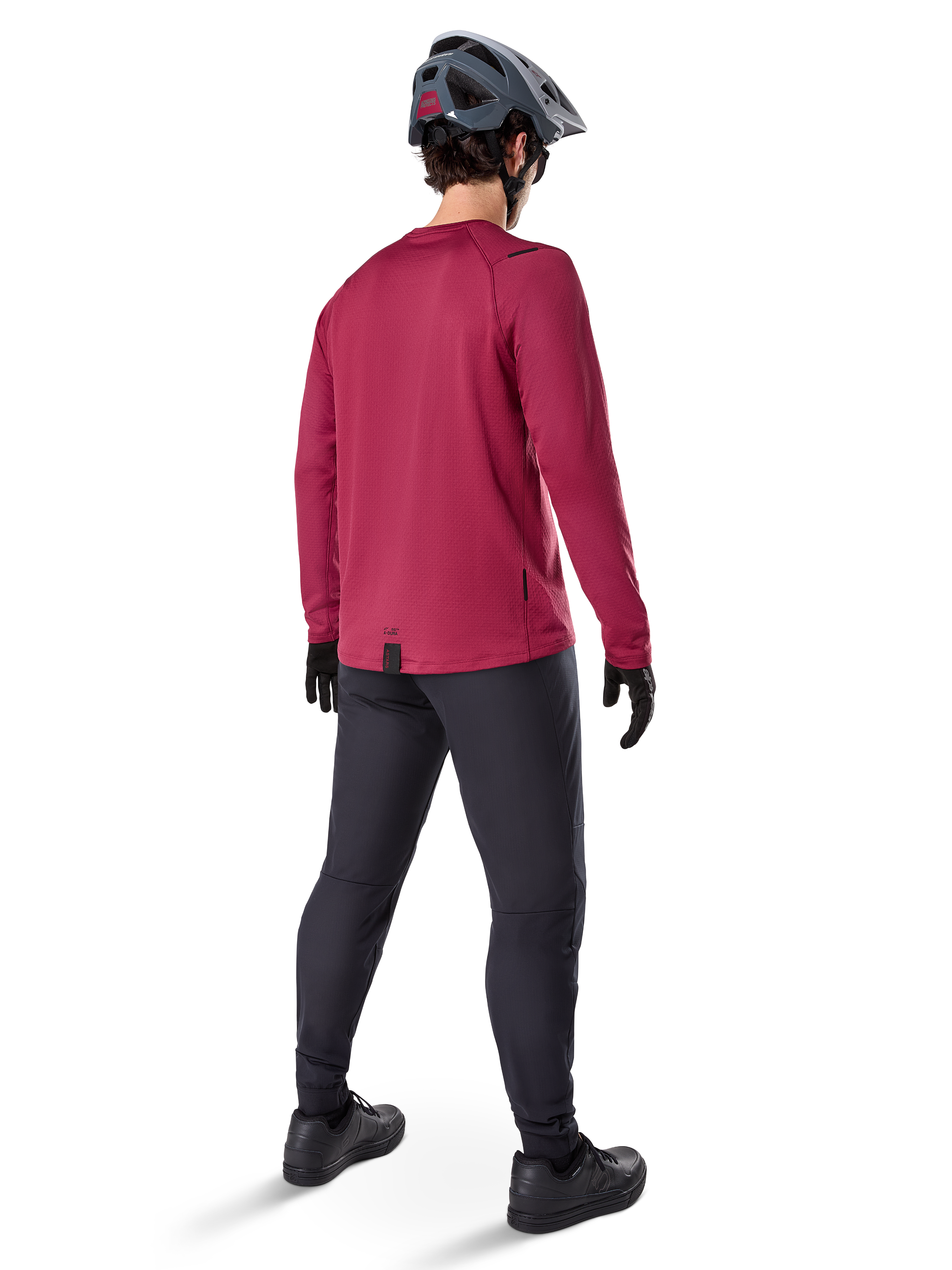 Alpinestars A-Dura Thermal Jersey, bordeauxrood wielershirt met lange mouwen, achteraanzicht, gedragen met een zwarte mountainbikebroek en een grijze helm, voorzien van een verlengde achterzoom voor extra dekking aan de achterkant, mountainbike-uitrusting voor koud weer