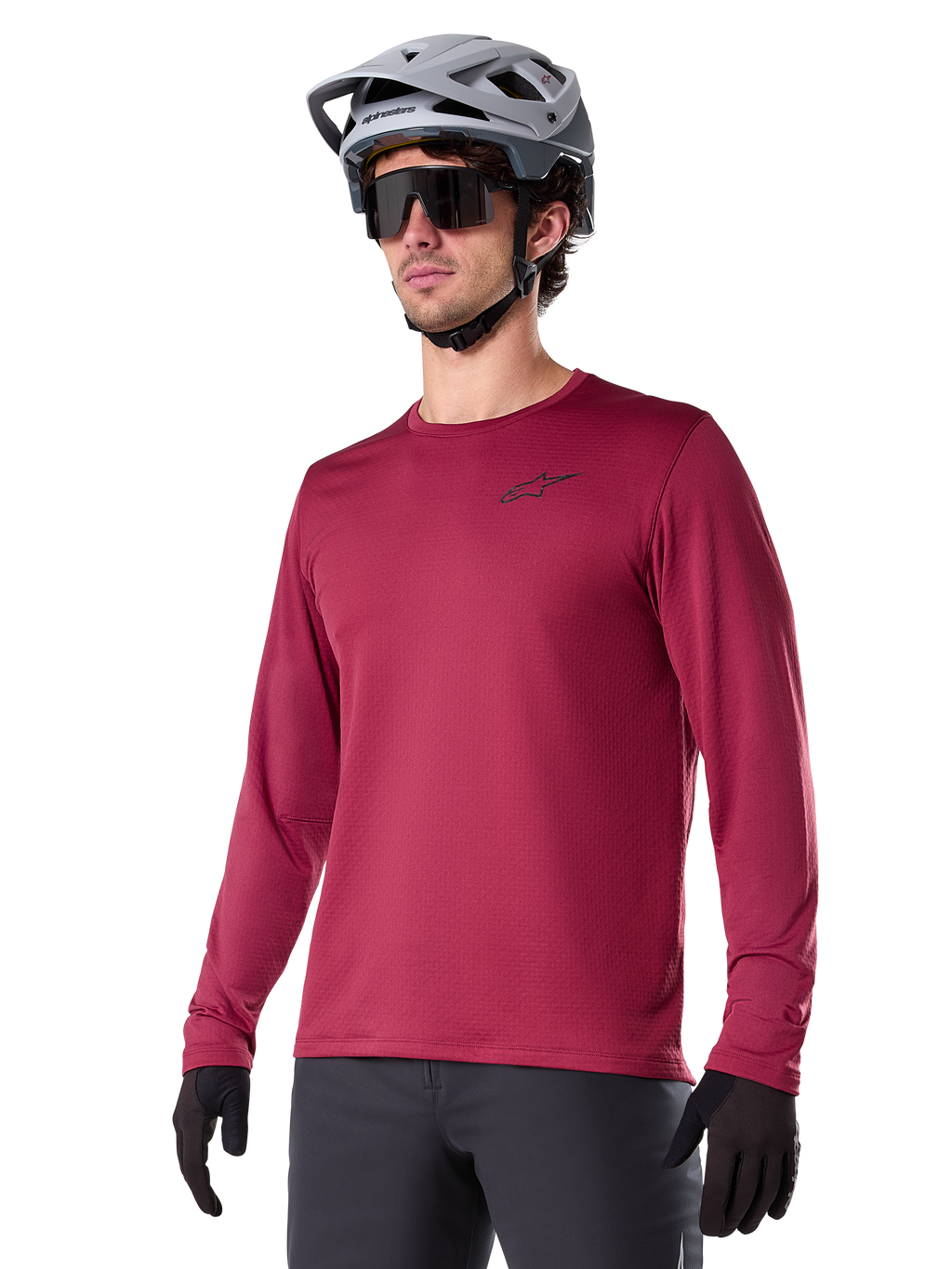 Alpinestars A-Dura Thermal Jersey, mountainbike-jersey met lange mouwen, bordeauxrood, voorzien van een geïsoleerde fleecevoering en klein zwart logo op de borst, gedragen met een grijze helm, zwarte zonnebril en zwarte handschoenen, ontworpen voor fietsen in koud weer