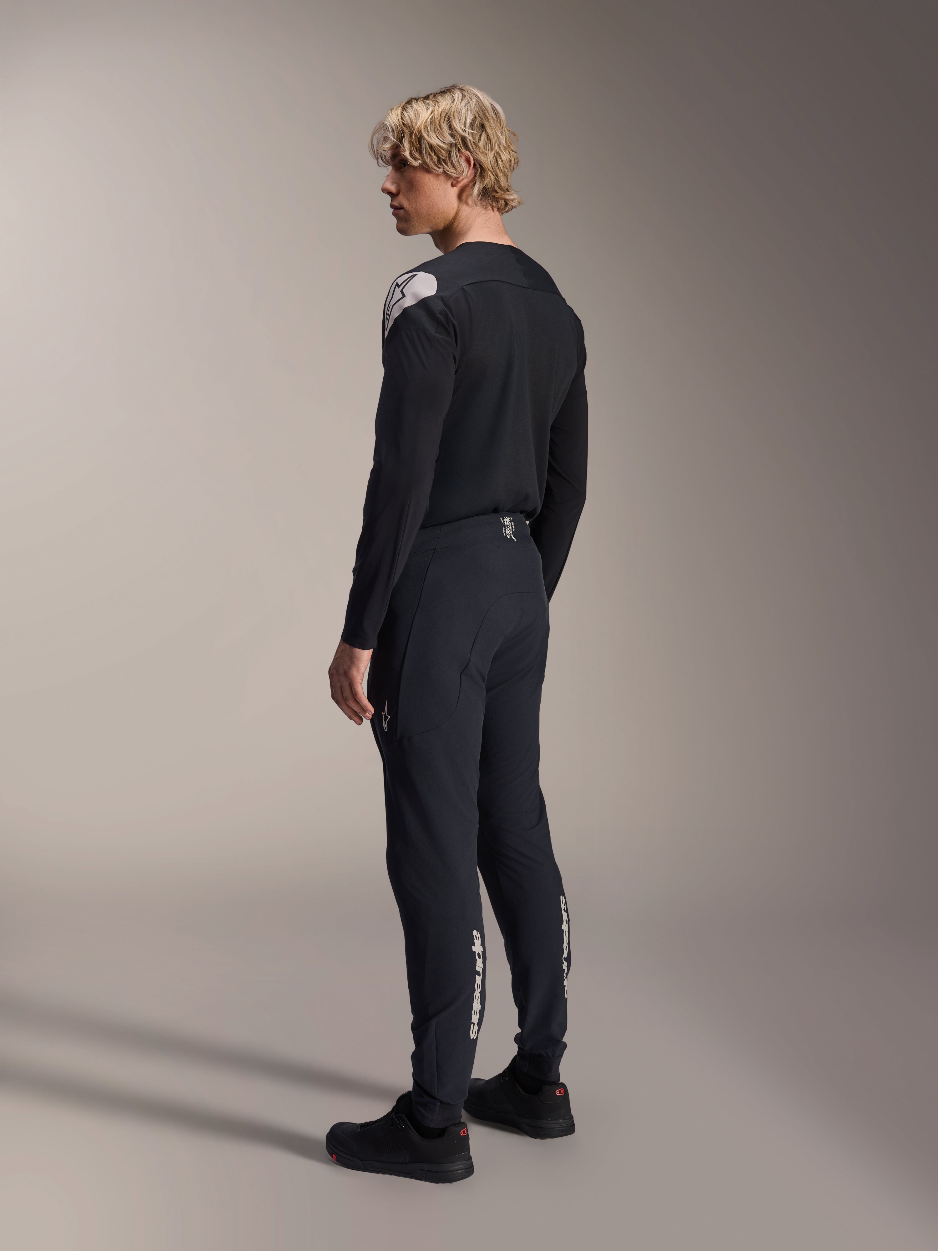 Alpinestars A-Aria Polartec Elite Jersey - Long Sleeve, Black, worn by a model from a back-side profile, featuring a white logo on the shoulder, paired with matching black cycling pants for a professional MTB outfit.