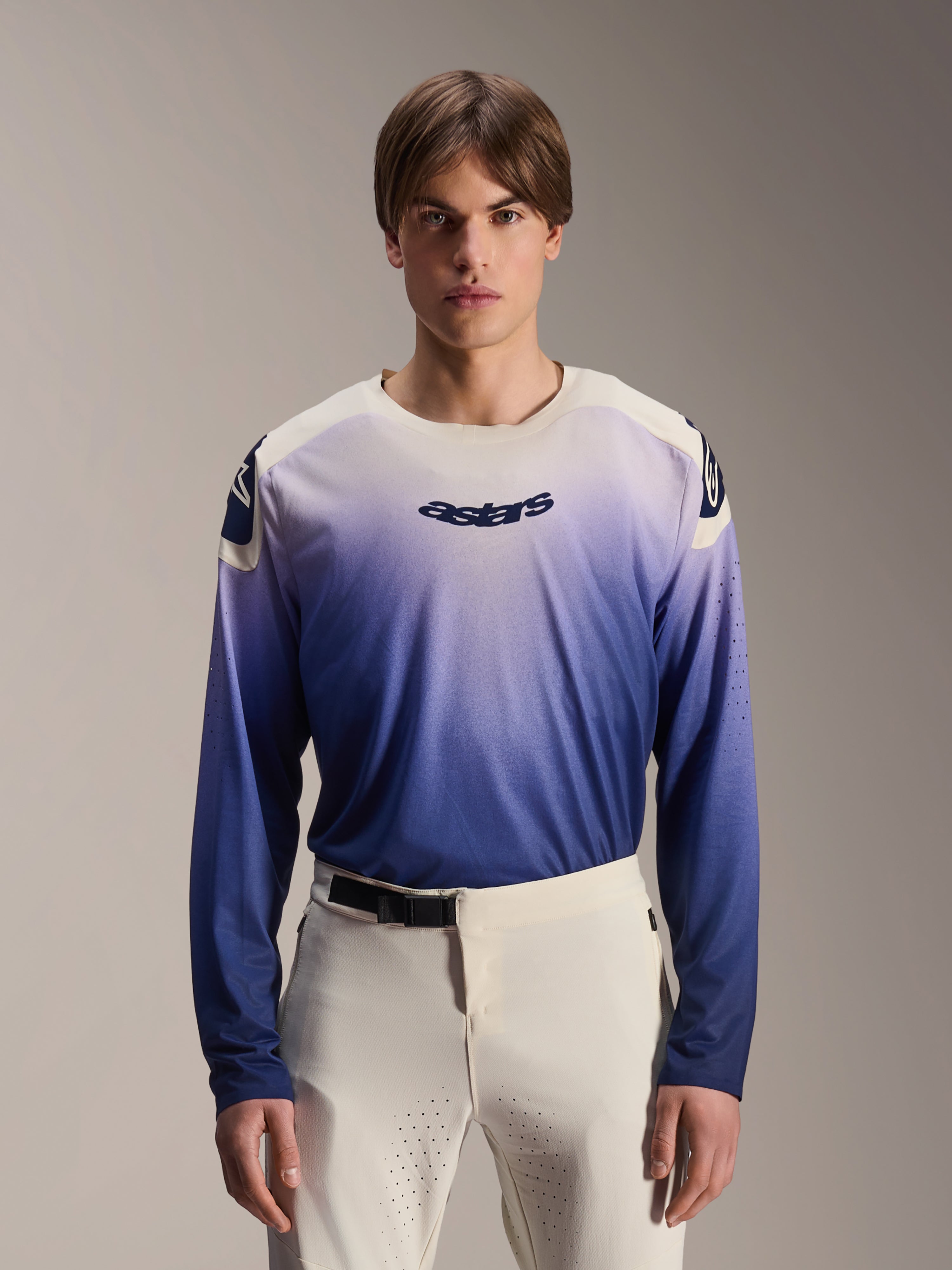 Alpinestars A-Aria Polartec Maker Elite jersey met lange mouwen, MTB-shirt, Baja Blue met een kleurverloop van wit naar blauw, gedragen door een model met een witte broek, donkerblauw logo op de borst en laserperforaties op de mouwen, technische mountainbikekleding