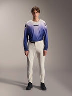 Alpinestars A-Aria Elite broek, ecru prestatiegerichte MTB-broek, gebroken witte fietsbroek met laser-geperforeerde dijpanelen en magnetische gesp, gedragen met blauw verloopshirt met lange mouwen en zwarte schoenen, prestatiepasvorm voor trailrijden