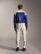 Alpinestars A-Aria Polartec Maker Elite Jersey met lange mouwen, Baja Blue en gebroken wit, achteraanzicht van model in technische mountainbike-uitrusting inclusief gebroken witte broek met Alpinestars-branding op de onderbenen, performance wieleroutfit voor off-road trails