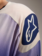 Alpinestars A-Aria Polartec Maker Elite Jersey, mountainbikeshirt met lange mouwen, Baja Blue en wit, close-up van de schouder met een groot blauw cirkelvormig Alpinestars-logo met een witte ster, met laserperforaties en technische stoftextuur