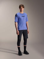 Mannelijk model draagt Alpinestars A-Aria Polartec Elite Short Sleeve Jersey in Baja Blue, gecombineerd met een zwarte MTB-short en kniebeschermers, voorzien van zwarte Astars-logo's op de borst en schouder, hoogwaardige mountainbike-uitrusting