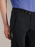 Alpinestars A-Aria Elite Shorts, mountainbikebroek, Black Titanium, voorzien van een magnetische gespsluiting, zak met rits en wit Alpinestars-logo, gedragen met een blauw fietsshirt, hoogwaardige mountainbike-uitrusting