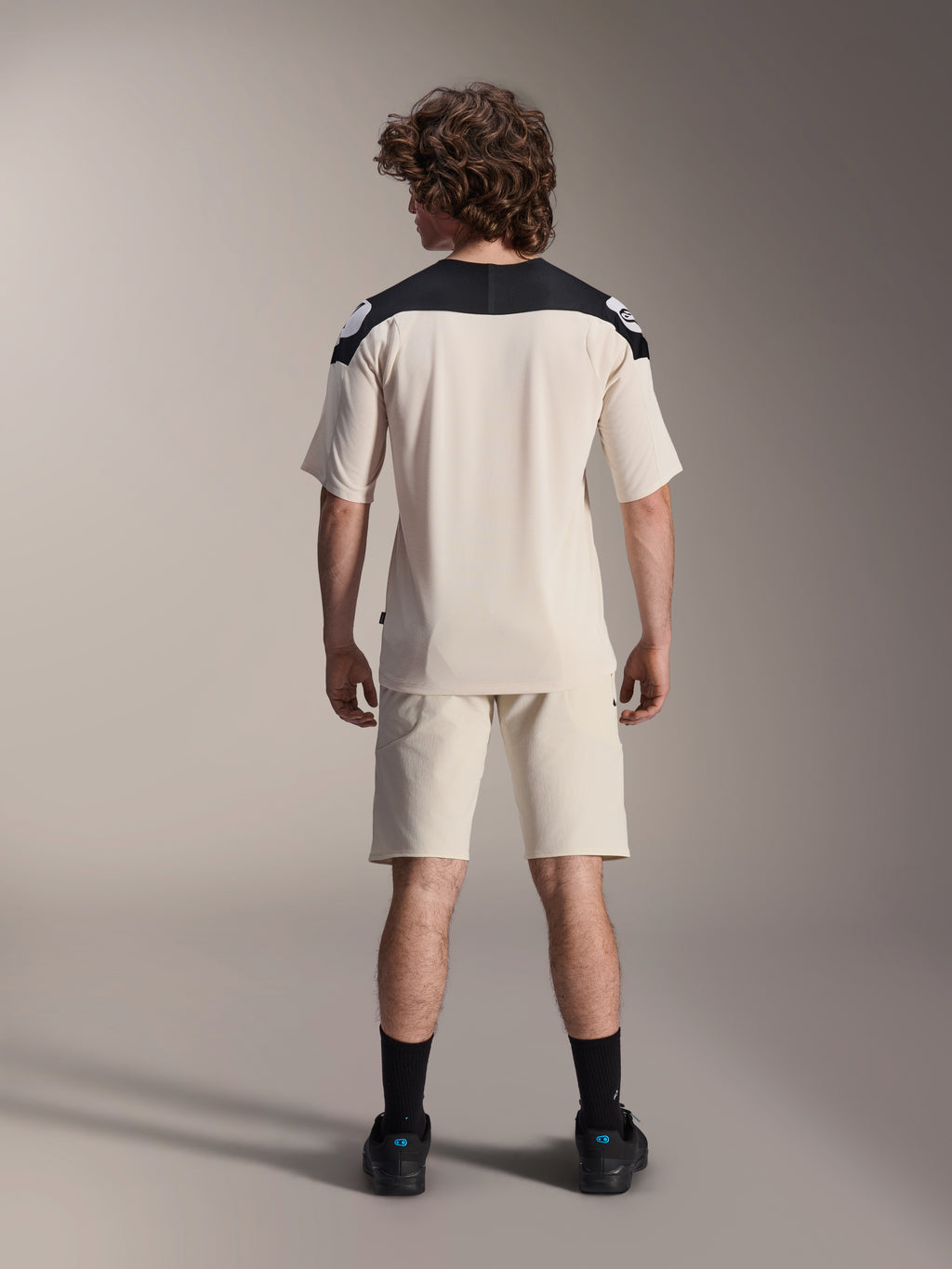 Alpinestars A-Aria Elite shorts en A-Aria Polartec Elite SS jersey, ecru met zwarte schouderpanelen, achteraanzicht van een model in mountainbike-performancekleding, gestyled met zwarte sokken en schoenen