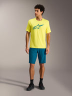 Gele Alpinestars A-Dura Ride SS jersey en groenblauwe shorts, performance mountainbikekleding in een studio.